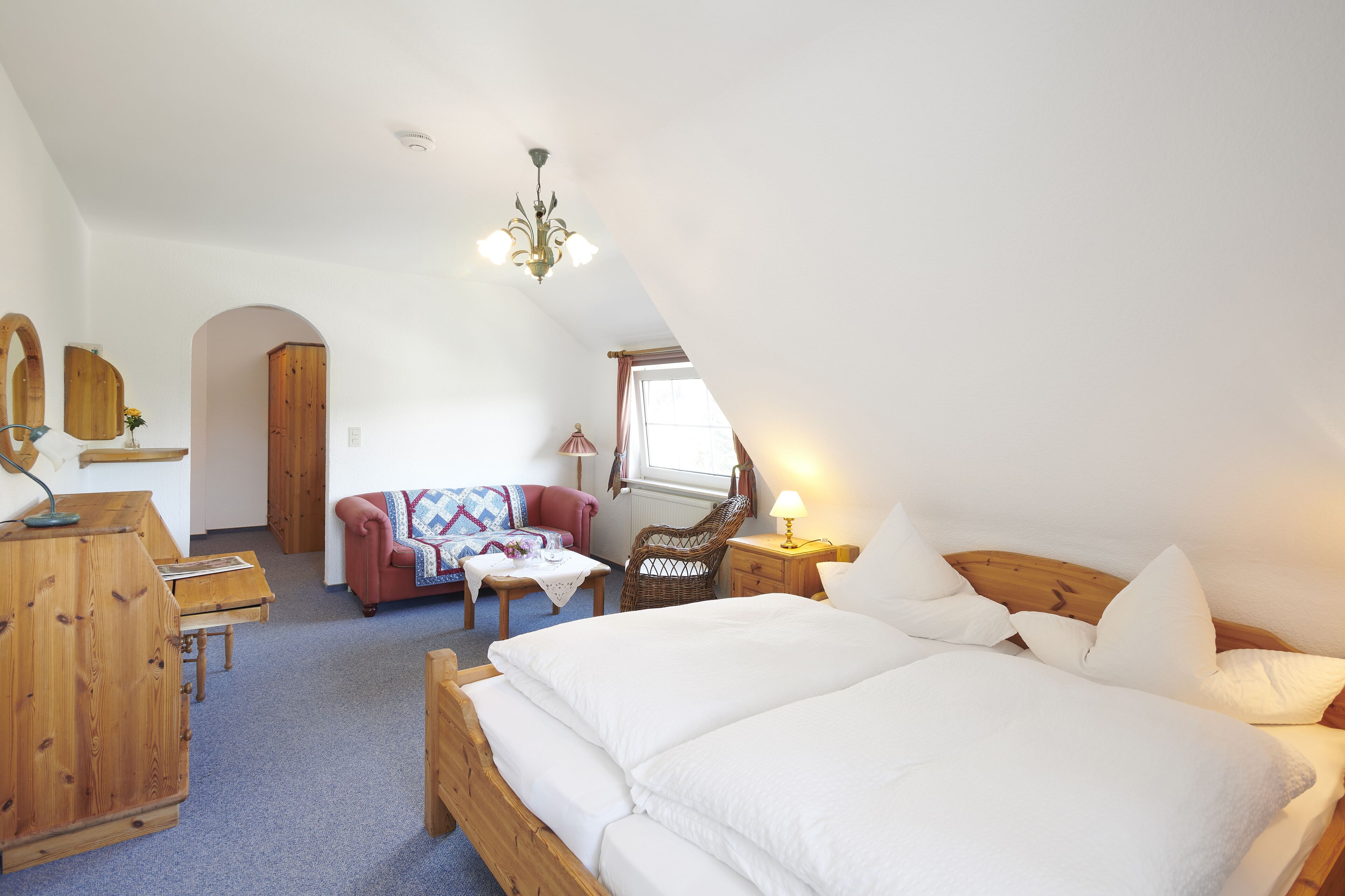 A cozy bedroom with a large bed, wooden furniture, a small table, and a chair.