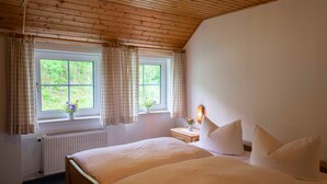 A bedroom with two beds, a window with curtains, a bedside table with a lamp, and a radiator. - B&B Sauerland TCF (Willingen)