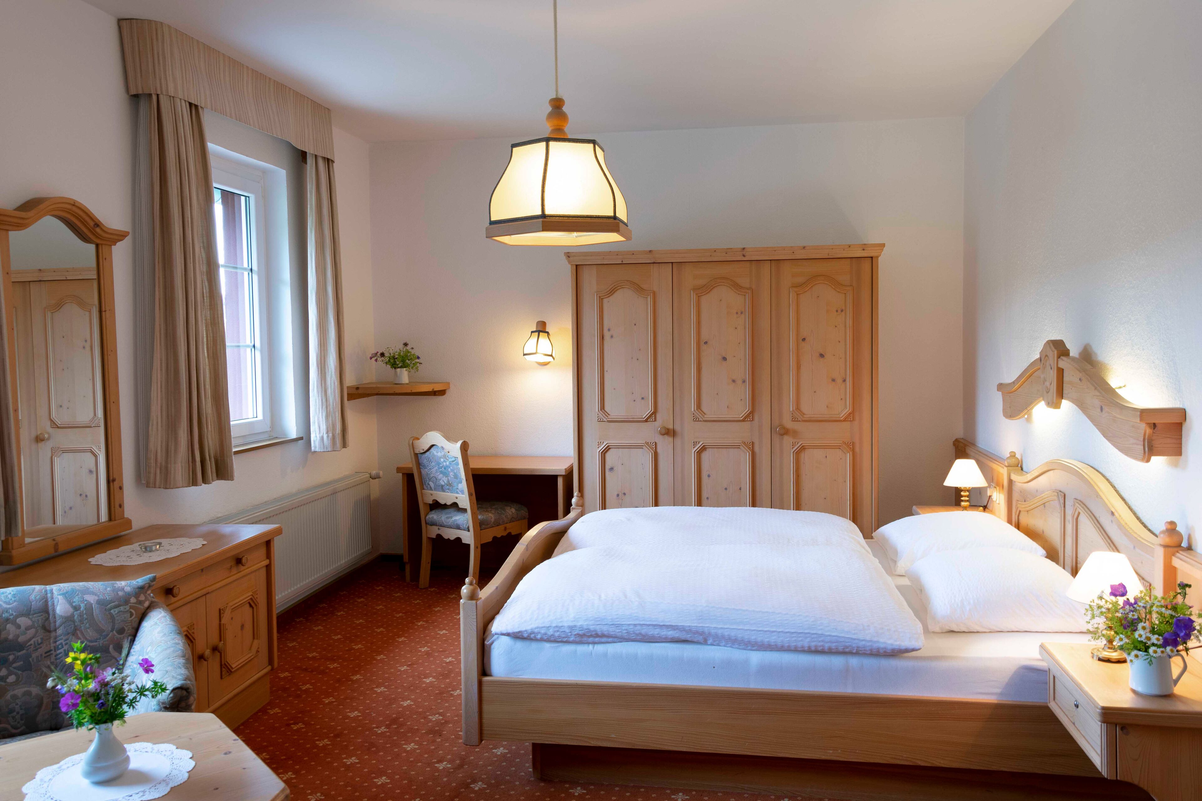 A bedroom with a wooden bed, a desk, a chair, a dresser, and a window with curtains.