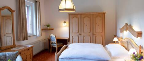 A bedroom with a wooden bed, a desk, a chair, a dresser, and a window with curtains.