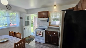 A kitchen with wooden cabinets, a stove, a refrigerator, and a dining table with chairs.