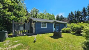 A small, single-story house with a blue exterior, a front porch, and a fenced yard.