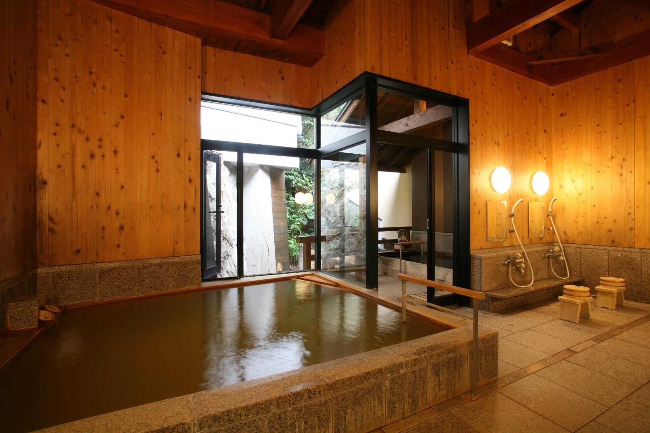 A wooden interior with a hot spring bath, stone flooring, and a glass door leading outside.