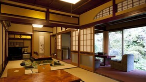 Ein traditioneller japanischer Raum mit Tatami-Boden, einem niedrigen Holztisch und Schiebetüren, die auf einen Balkon mit Blick auf Grün führen.