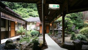 Ein traditioneller japanischer Garten mit einem Pfad, Holzbauten und einem Schild, das den Ausgang weist.