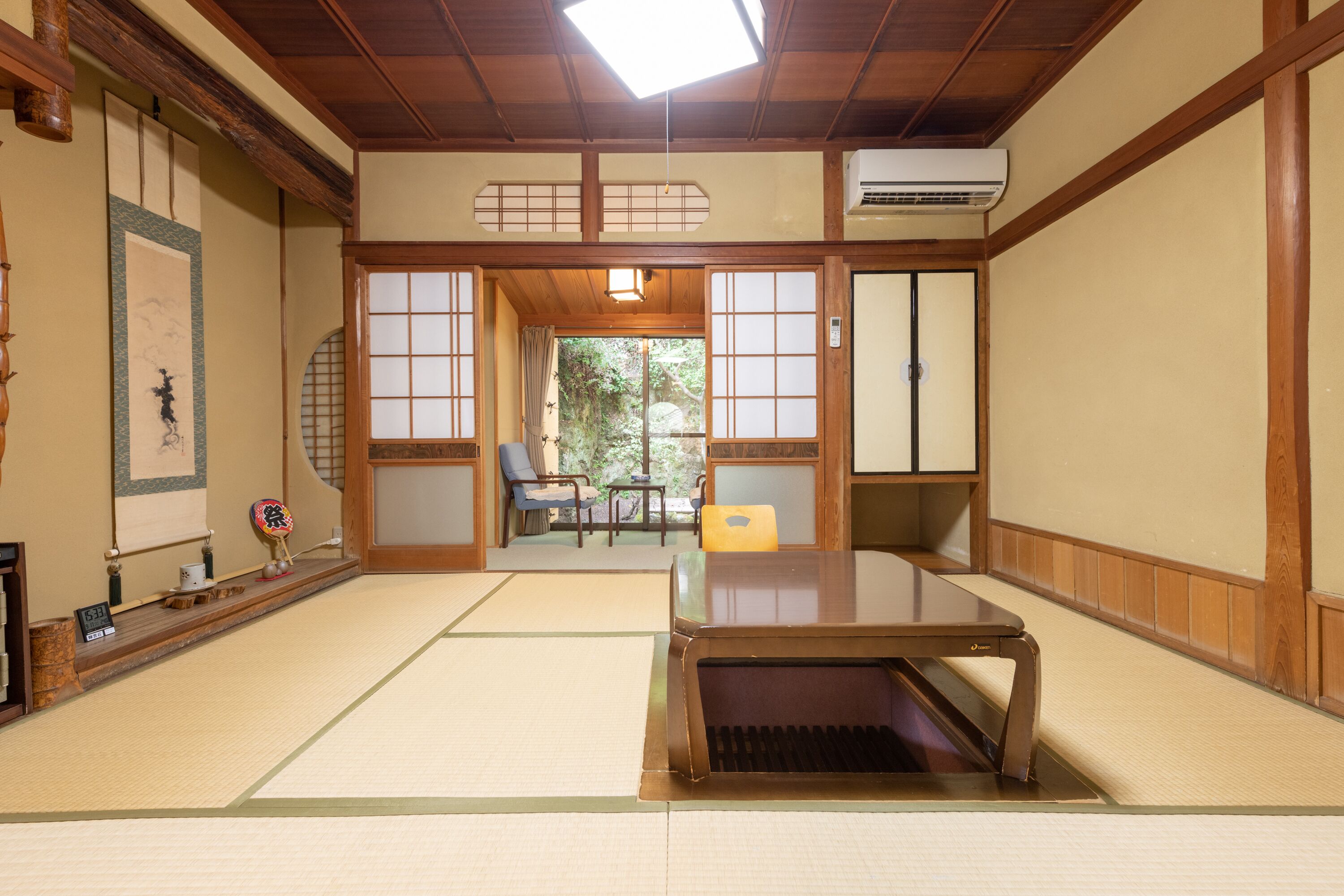 A traditional Japanese room with tatami flooring, a low table, sliding doors, and a view of greenery outside.