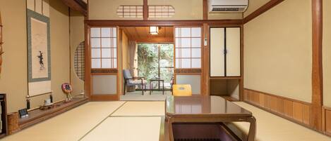 A traditional Japanese room with tatami flooring, a low table, sliding doors, and a view of greenery outside.