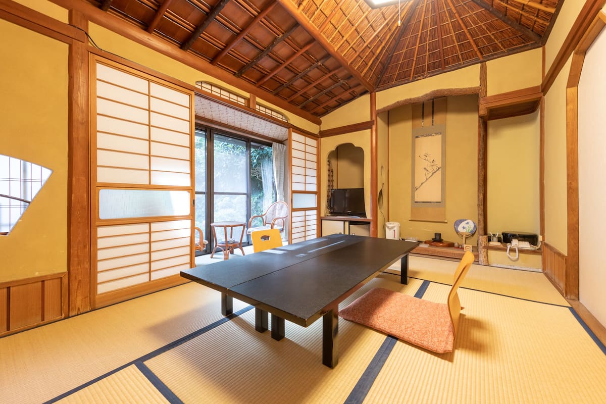 A tatami mat room with a low table, a wooden chair, and sliding doors.