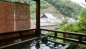 Ein traditionelles japanisches Onsen mit einer Holzterrasse und Blick auf einen Tempel im Hintergrund.