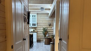 A wooden interior hallway leading to a kitchen area with a dining table, chairs, and a potted plant.