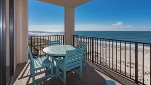A balcony with a table and chairs, overlooking a beach with a clear view of the ocean.