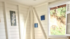 Un dormitorio con cama, ventana con vistas a la vegetación y un cuadro floral en la pared.