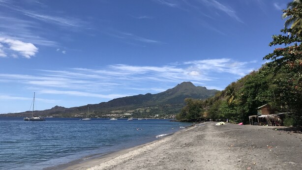 Una playa con barcos, una montaña y una cabaña con techo de paja.
