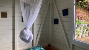 Una habitación con una cama, mosquitero colgante y ventana con vista a un jardín.