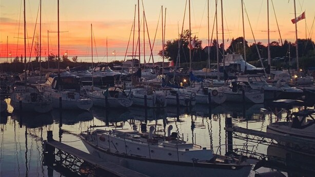 Un puerto deportivo con varios veleros amarrados al atardecer.