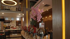 A modern hotel lobby with a reception desk, a coffee station, and a decorative floral arrangement.