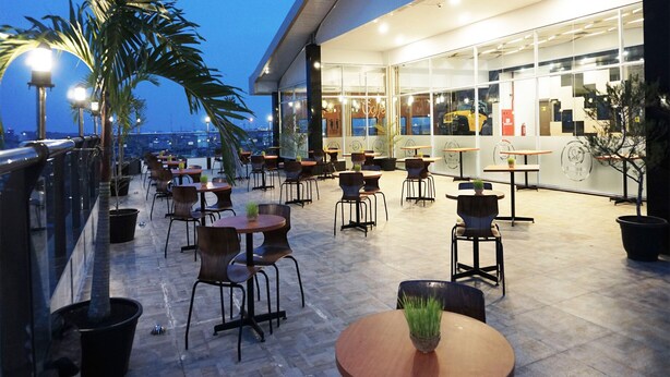 An outdoor café area with tables and chairs, potted plants, and a view of the cityscape.