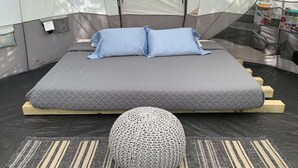 A tented room with a bed, pillows, a knitted pouf, and a mat. - Comfy Camping At The Palms (Old Town)
