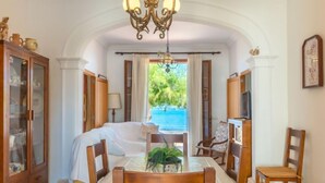 Ein Zimmer mit Esstisch, Stühlen, einer Kristallleuchtre, Meerblick und einer Vitrine.