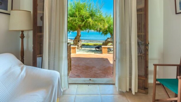 Ein Zimmer mit einem Bett, einem Sessel und Meerblick durch eine offene Tür.