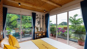 A bedroom with a large bed, a desk, and a view of a garden through large windows. - An Thai Bar & Homestay (Hoa Lu)