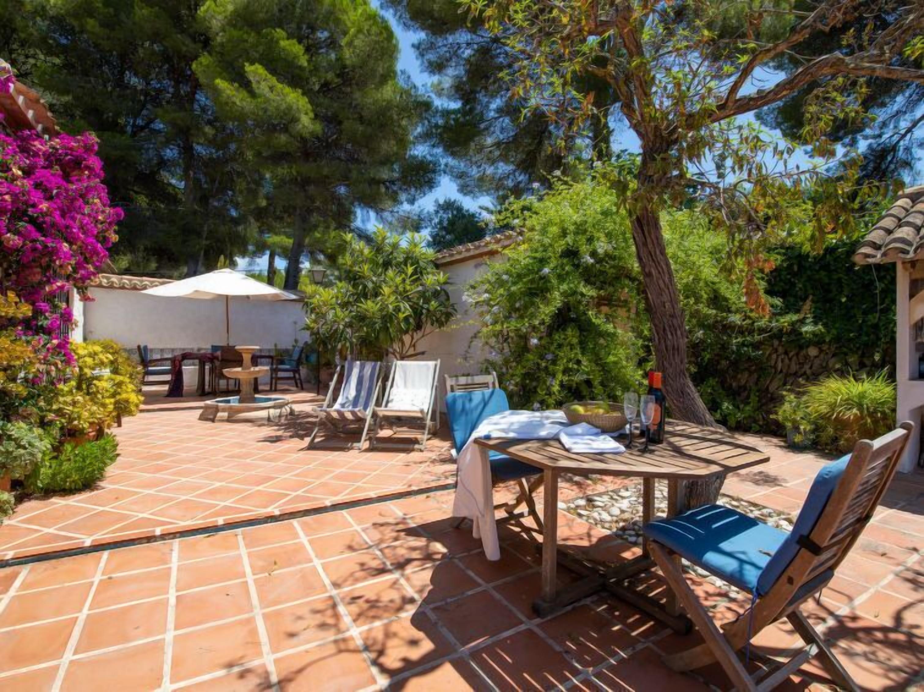 An outdoor patio with a tiled floor, a table with chairs, and a pergola with a white umbrella.
