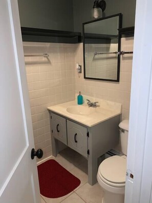 A bathroom with a white sink, a mirror above it, and a toilet. There is a red rug on the floor. - Ackwood Lodge - The Cottage (Bass Lake)