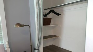 Un dormitorio con cama, mesita de noche, lámpara y armario con estantes y espacio para colgar.