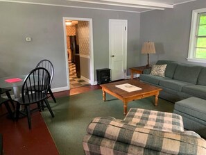 A living room with a sofa, a plaid ottoman, a coffee table, a lamp, and a fireplace. - Ackwood Lodge - The Cottage (Bass Lake)