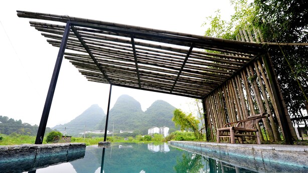 A tranquil pool area with a bamboo pergola, clear water reflecting the surroundings, and a mountain backdrop.