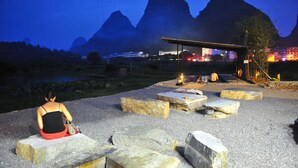 A person sitting on a stone bench with a view of mountains and a building in the background.
