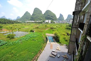 A view of a lush green landscape with a pool area, bamboo structures, and distant mountains. - Yangshuo Sudder Street Guesthouse (Guilin)