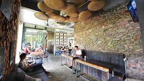A cafe with a stone wall, wooden tables, and woven ceiling lamps.