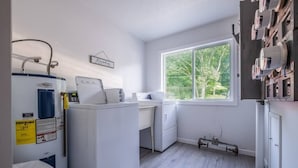 Ein Waschraum mit Waschmaschine, Trockner und einem Fenster mit Blick auf Bäume.