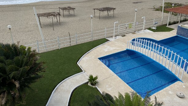 A beachside pool area with a view of the ocean, a fenced pool, and a few beach umbrellas. - Villas del Pacifico | Habitación Privada #4  (El Carrizal)