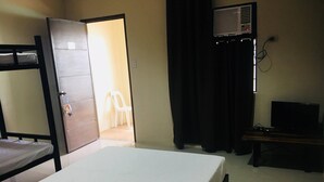 A hotel room with a bed, a desk with a computer, a chair, and an open door leading to another room. - Hacienda Galea Resort and Events Place (Baliuag)