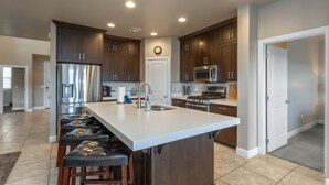 A modern kitchen with dark wood cabinets, stainless steel appliances, and a central island with bar stools. - Poolside 4 bdr near OHV Trails w/ Game Room (Washington)