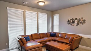 A corner living room with a brown leather sectional sofa, a patterned rug, and a wall art piece. - Poolside 4 bdr near OHV Trails w/ Game Room (Washington)
