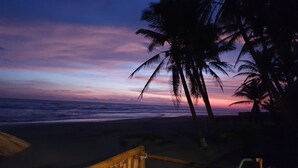 A beach scene with a wooden structure, palm trees, and a sunset. - La Perla Playa Azul Bungalow #1 (Playa Azul)