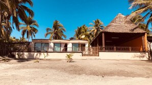 A beachfront property with a thatched-roof structure, a covered outdoor area, and a building with multiple windows. - La Perla Playa Azul Bungalow #1 (Playa Azul)