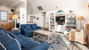 A living room with a blue sofa set, a coffee table, a bookshelf, and a television. - Shell's Shack: Oceanside, Private Pool, Hot Tub, Tiki Bar, Putting Green (Corolla)