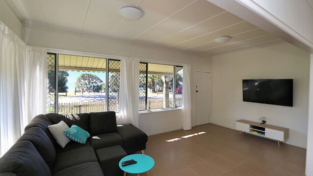 A living room with a sectional sofa, a TV mounted on the wall, and large windows with a view of the outside. - Beach Shack On 115 Esplanade (BARGARA)