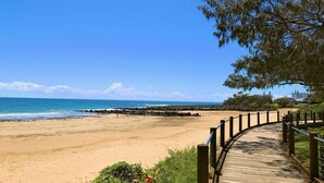 A beach with a wooden boardwalk leading to the shore, surrounded by greenery and a clear blue sky. - Beach Shack On 115 Esplanade (BARGARA)