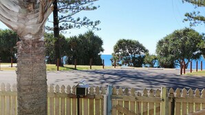 A paved road with a wooden fence, trees, and a clear sky. - Beach Shack On 115 Esplanade (BARGARA)