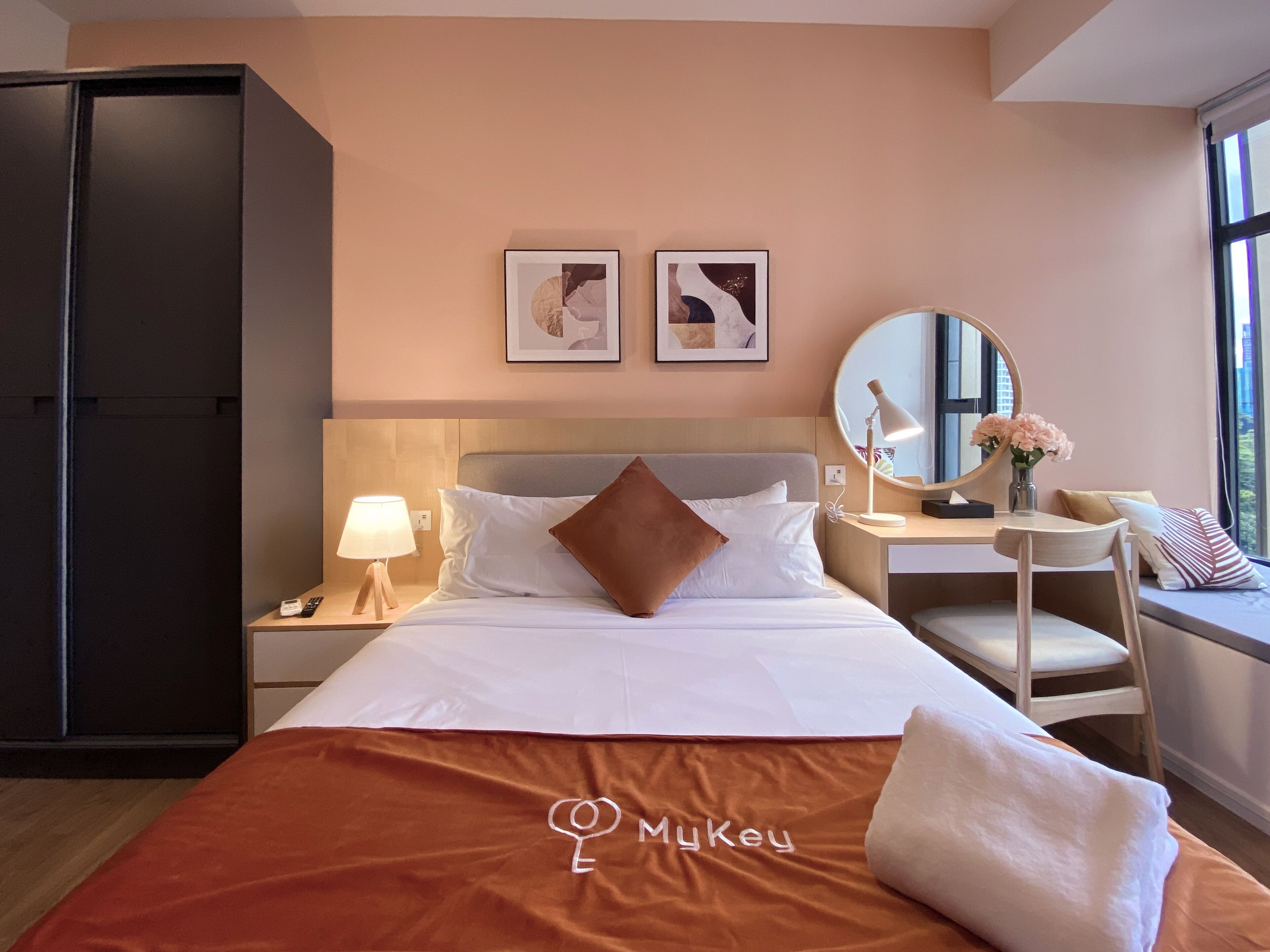 Ein Hotelzimmer mit einem Bett, einem Schreibtisch, einem Stuhl, einem Kleiderschrank, einem Nachttisch mit Lampe und zwei gerahmten Bildern an der Wand.