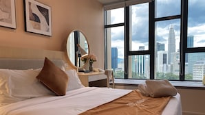 A hotel room with a large bed, a desk, a mirror, and a window with a city view.