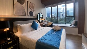 Habitación de hotel con una cama grande, un escritorio con silla, ventana con vistas a la ciudad y obras de arte en la pared.