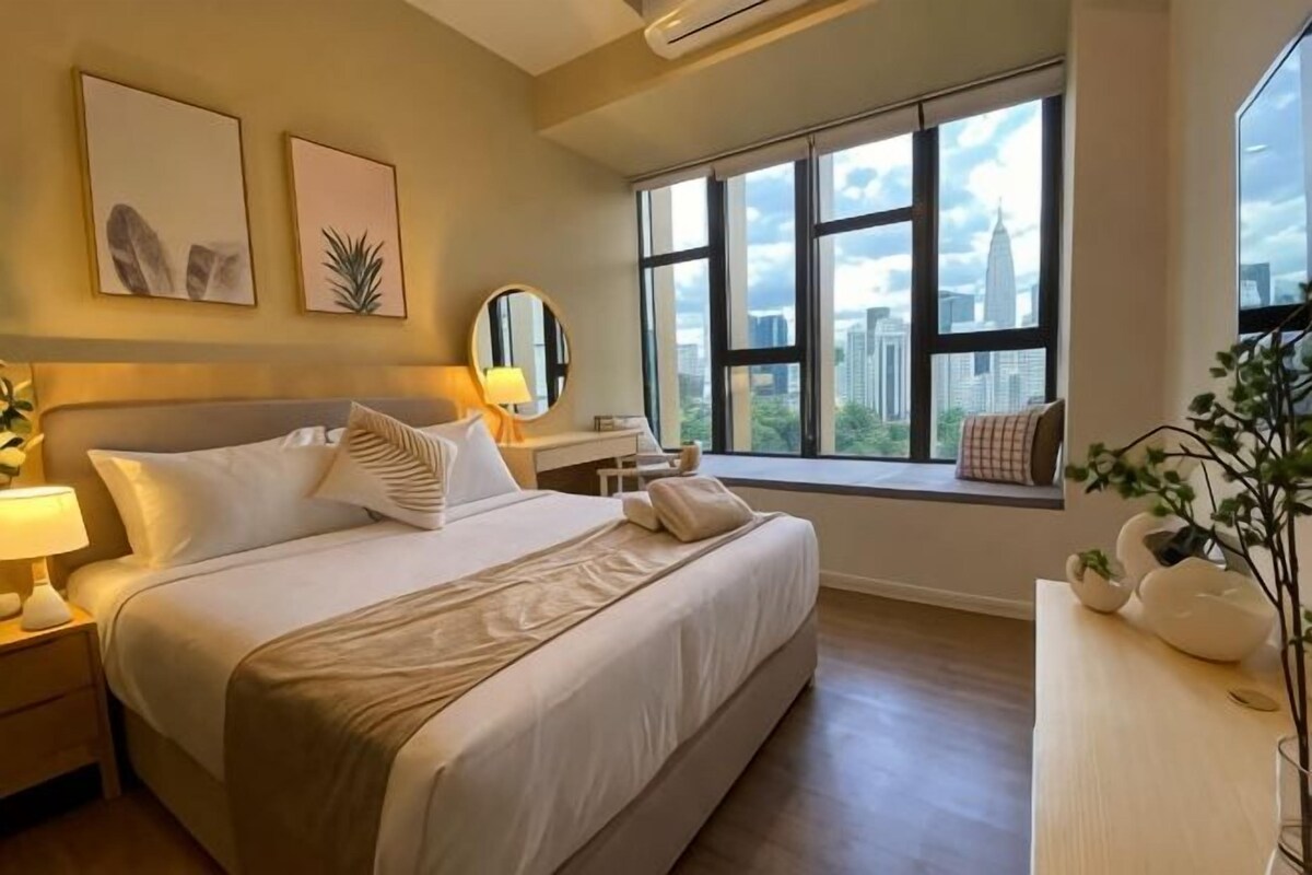 Une chambre avec un grand lit, une table de chevet, un bureau et une fenêtre donnant sur la ville.