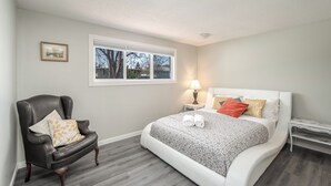 Une chambre à coucher avec un lit, une chaise, une table de chevet, une lampe et une fenêtre.