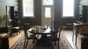Comedor con una mesa redonda, sillas, un tapete estampado y dos ventanas con persianas.